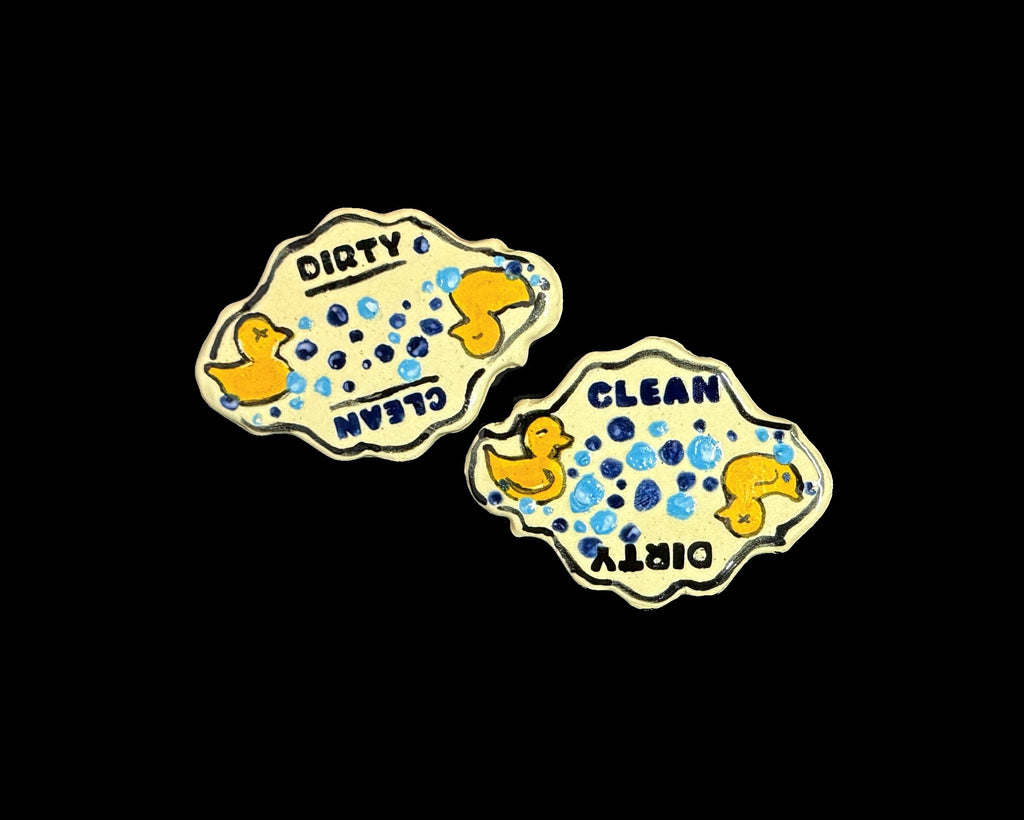 Two decorative magnets reading 'DIRTY CLEAN' and the other 'CLEAN DIRTY', featuring yellow rubber duckies and blue soap bubbles on a black background.